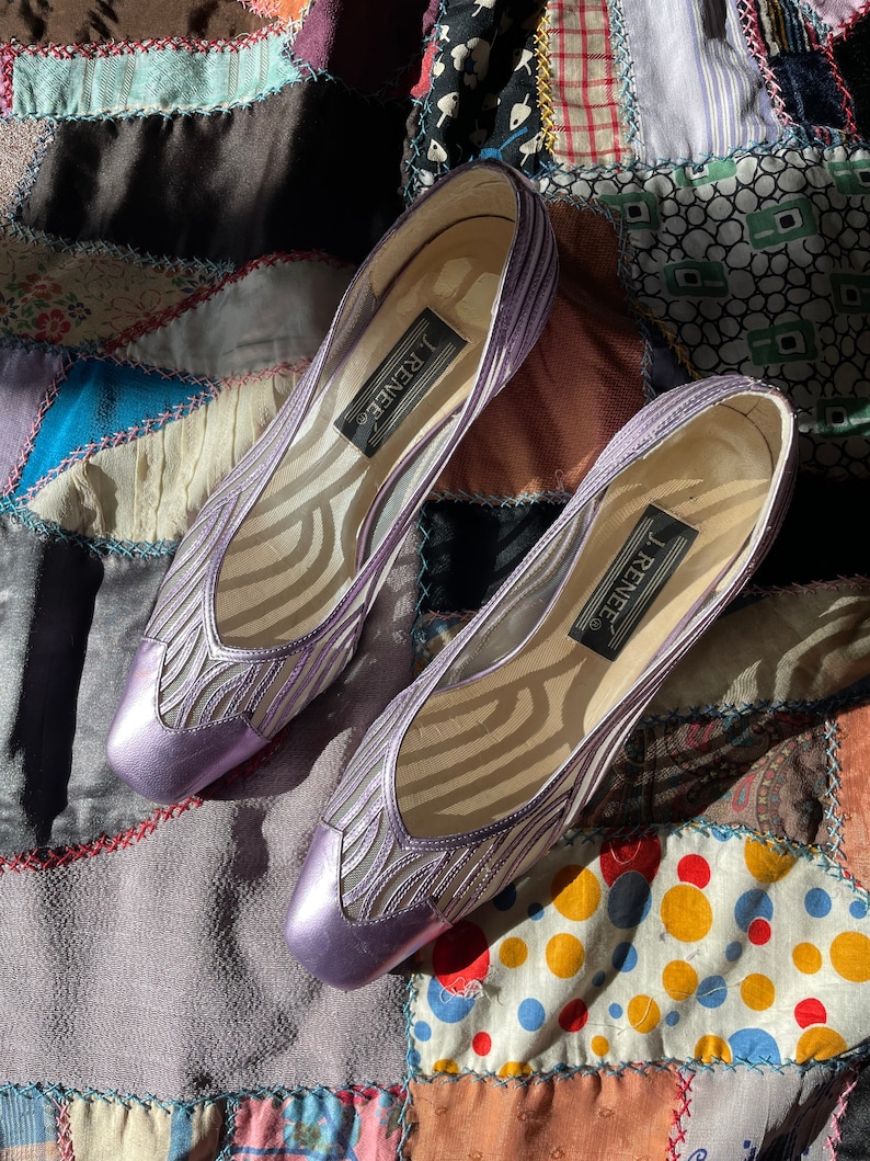 Pu&ograve; includere: Un paio di scarpe con tacco in rete e pelle lavanda con punta quadrata. Le scarpe hanno un motivo delicato e il nome del marchio "J. Renee" &egrave; stampato sulla soletta.
