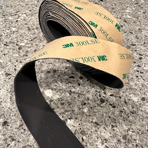 May include: A roll of black adhesive tape with a brown backing. The tape is labeled "3M 300LSE".