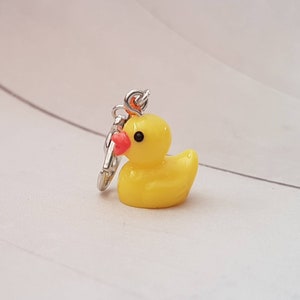 May include: A yellow rubber ducky keychain with a silver chain and a red beak.