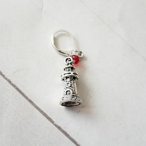 May include: Silver lighthouse charm with a red bead, used as a stitch marker for knitting or crocheting.