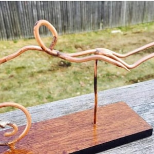 May include: A copper wire sculpture of a person swimming, mounted on a wooden base. The sculpture is made of thin wire and is very detailed.