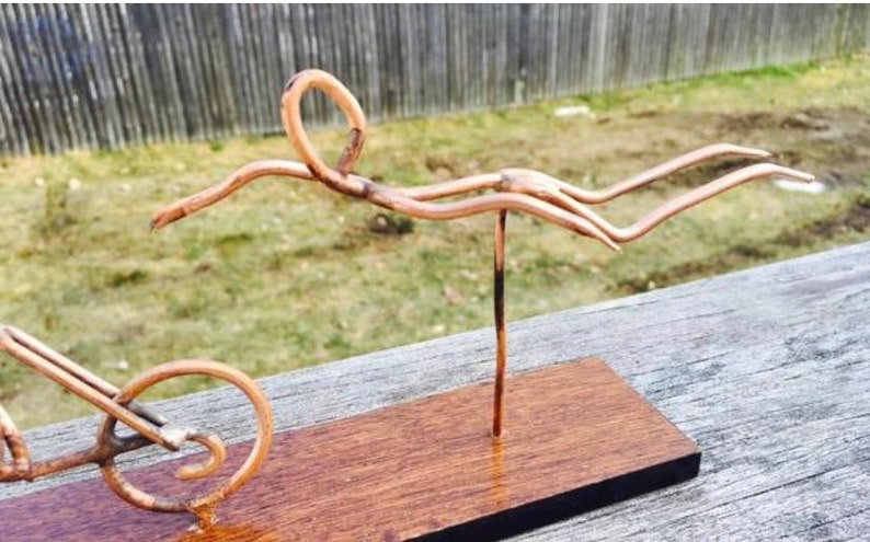 May include: A copper wire sculpture of a person swimming, mounted on a wooden base. The sculpture is made of thin wire and is very detailed.