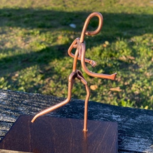 May include: A copper wire sculpture of a person running, mounted on a dark brown wooden base.