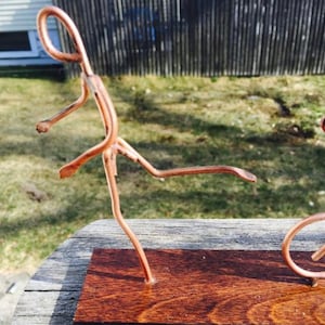 May include: A copper wire sculpture of two figures, one kicking a ball, the other riding a bicycle, on a wooden base.