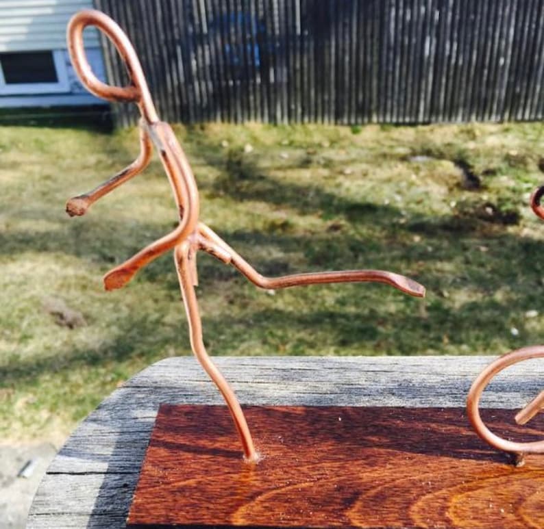 May include: A copper wire sculpture of two figures, one kicking a ball, the other riding a bicycle, on a wooden base.