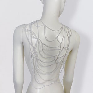 Può includere: Una collana bianca di perline con un design a rete. La collana è indossata da un manichino bianco.