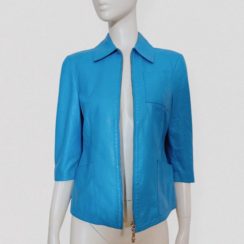 May include: A bright turquoise jacket with a collar, three-quarter sleeves, and a full-length zipper. The jacket has two front pockets and a single pocket on the chest. The jacket is displayed on a mannequin.