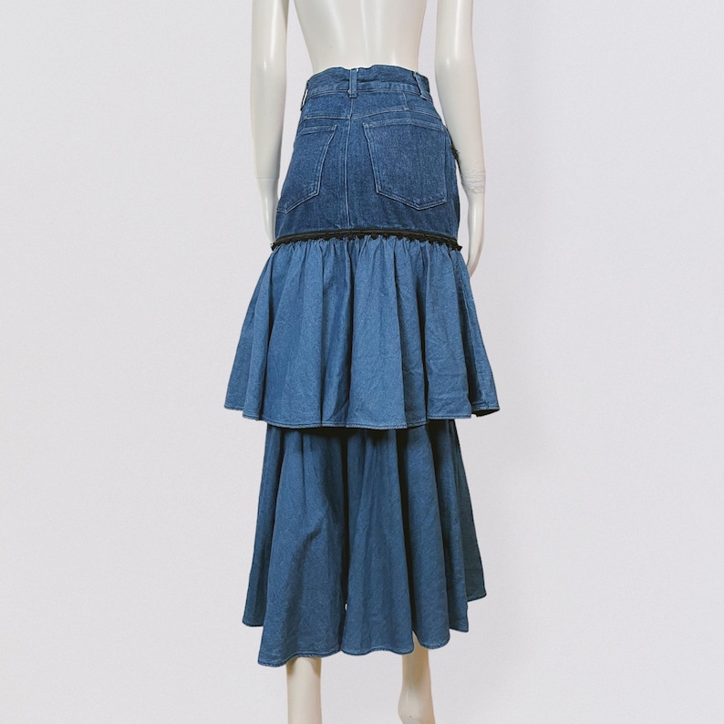 Pode incluir: Uma saia de ganga com um design de babados em camadas. A saia &eacute; de cor azul escura e tem uma guarni&ccedil;&atilde;o preta em torno do babado superior.