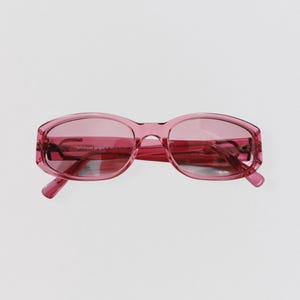 Peut inclure: Lunettes de soleil roses avec une monture rectangulaire. Les verres et la monture sont d'une teinte rose assortie. Les lunettes de soleil ont un design classique et rétro.