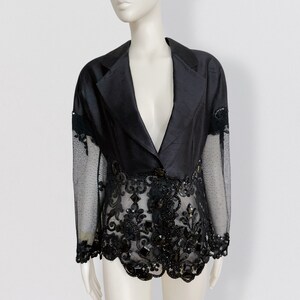 Peut inclure: Un blazer noir avec une superposition de dentelle transparente ornée de perles et de paillettes noires. Le blazer a un col classique à revers et une fermeture à un seul bouton.