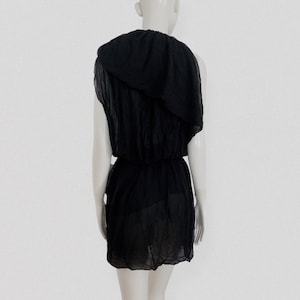 May include: A black, one-shoulder dress with a draped neckline and a cinched waist. The dress is made of a lightweight, semi-sheer fabric. The dress is displayed on a mannequin against a white background.