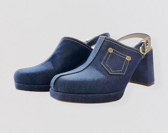 May include: A pair of denim clogs with a platform sole and a high block heel. The blue denim shoes feature a pocket design with yellow stitching and a gold-tone buckle on the ankle strap. The clogs have a heel height of approximately 4 inches.