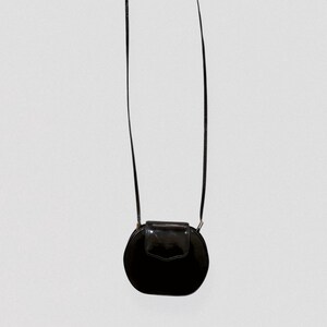 May include: A black, round crossbody bag with a glossy finish. The bag features a flap closure and a long, thin strap. The design is simple and elegant, suitable for various occasions.