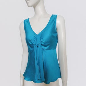 May include: A sleeveless turquoise blue silk top with a ruffled detail at the neckline.