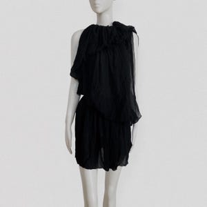 May include: A black dress with a layered, asymmetrical design. The top features a ruffled, off-the-shoulder detail, and the skirt is a simple, gathered style. The dress is made of a lightweight, flowing fabric, perfect for a special occasion.
