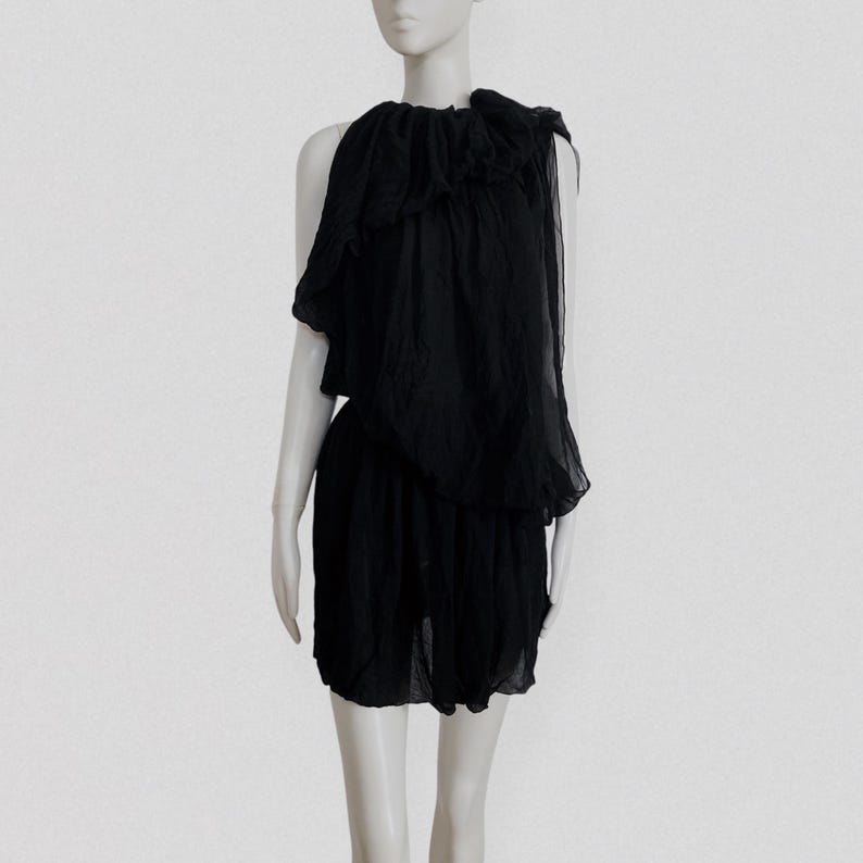 May include: A black dress with a layered, asymmetrical design. The top features a ruffled, off-the-shoulder detail, and the skirt is a simple, gathered style. The dress is made of a lightweight, flowing fabric, perfect for a special occasion.