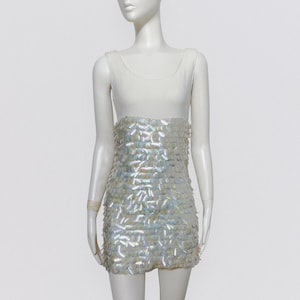 Peut inclure: Une robe blanche sans manches avec un haut blanc et une jupe en sequins irisés.