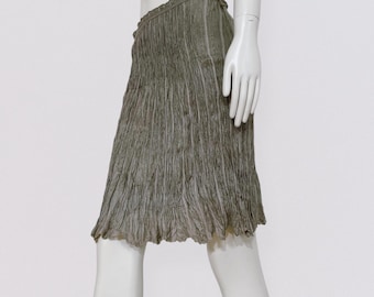 May include: A sage green skirt with a textured, pleated design. The skirt is knee-length and has a ruffled waistband. The fabric appears to be lightweight and flowing, suitable for warm weather.