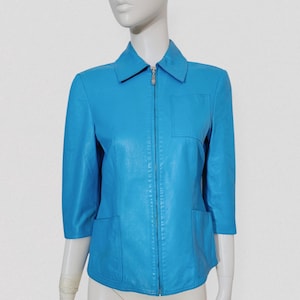 May include: A bright turquoise leather jacket with a collared neckline, a front zipper, and three-quarter sleeves. The jacket has two front pockets and a tailored fit. The jacket is displayed on a mannequin.