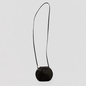 May include: A black, oval-shaped crossbody bag with a long, thin strap. The bag has a glossy finish and a small, rectangular clasp. The strap is attached to the bag with small gold-colored hardware.