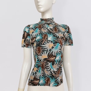 Może przedstawiać: Koszulka z krótkim rękawem i golfem w abstrakcyjny wzór w kolorze brązowym, niebieskim i białym. Wzór przedstawia wirujące, przypominające liście kształty.
