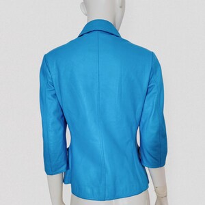 May include: A bright turquoise leather jacket with three-quarter sleeves and a notched collar. The jacket is displayed on a mannequin, showcasing its tailored fit and design. The back view highlights the seams and structure of the garment.
