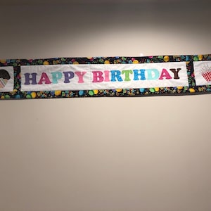 May include: A black and white banner with the words "Happy Birthday" in colorful letters. The banner has a black background with confetti and balloons. There are two cupcakes on each end of the banner.