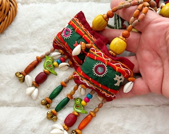 May include: Two green fabric pouches with colorful embroidery and mirrors, hanging from a beaded string with wooden beads, shells, bells, and small bird charms.