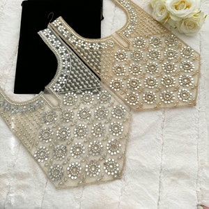 Op de afbeelding: Twee delicate, doorschijnende, parelversierde halslijnen met een bloemenmotief. De halslijnen zijn gemaakt van een fijn gaas en zijn versierd met kleine, ronde parels en pailletten. De parels zijn in een cirkelvormige patroon gerangschikt, waardoor een bloemenmotief ontstaat. De halslijnen zijn licht goud van kleur en hebben een subtiele glans.