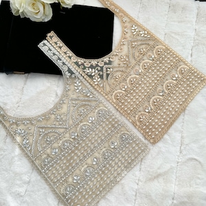 May include: Two beaded fabric embellishments in a light beige and a darker beige color. The embellishments are made of a mesh fabric with a variety of beads and sequins sewn on. The embellishments are shaped like a rectangle with a rounded top.
