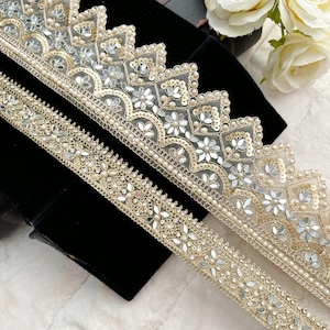 May include: Two pieces of gold and silver trim with a scalloped edge and pearl accents. The trim is decorated with small mirror-like sequins and floral designs.