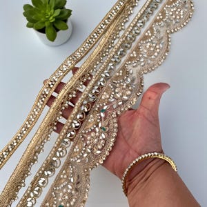 Puede incluir: Primer plano de varios adornos decorativos dorados con diseños intrincados. Los adornos presentan adornos como pedrería y perlas. También se ve una pulsera dorada. Una pequeña planta suculenta en maceta está en el fondo.
