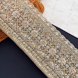 May include: Gold and white beaded trim with a scalloped edge. The trim features a repeating pattern of floral and geometric designs.