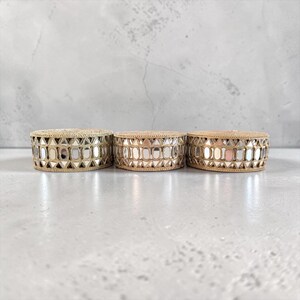 Puede incluir: Tres cajas decorativas redondas con detalles de espejo. Las cajas tienen una banda tejida de color natural alrededor de los lados y una parte superior a juego. Los detalles de espejo tienen varias formas geométricas, reflejando la luz.