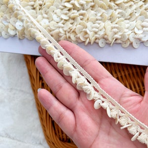 以下が含まれることがあります： 白いトリムに、小さな白い貝殻のようなビーズの列と、大きな白い貝殻のようなビーズの列が並んでいます。