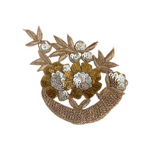 May include: A gold and silver floral applique with sequins and beads. The applique features a cluster of flowers with leaves and a curved base.