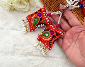 May include: Two colorful embroidered fabric pillows with white shell beads hanging from the bottom. The pillows are red, black, green, blue, and orange with a mirror in the center of each pillow.