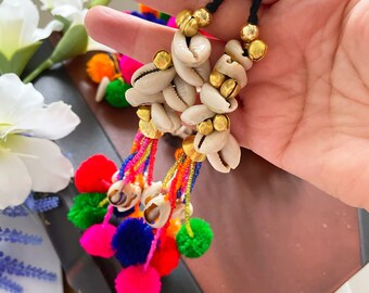 May include: Two colorful tassel keychains with white seashells and gold beads. The tassels are made of multi-colored yarn and pom-poms.