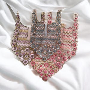 Puede incluir: Tres piezas de tela bordadas con motivos florales y en zigzag. Las piezas presentan un borde festoneado y están adornadas con cuentas y lentejuelas. La paleta de colores incluye tonos rosas, morados y azules.