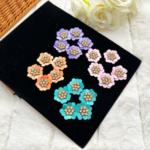 May include: Assortment of colourful flower-shaped embellishments with rhinestone accents. The embellishments are in shades of pink, purple, blue, and orange.