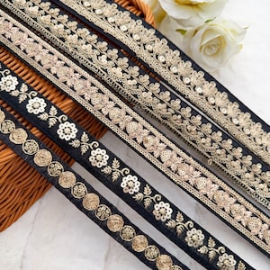 Può includere: Cinque passamanerie di nastro nero con ricami dorati e paillettes. Le passamanerie presentano diversi disegni, tra cui motivi floreali, cerchi e forme geometriche.