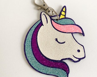 May include: A sparkly blue, purple, and pink unicorn head keychain with a silver key ring. The unicorn has a yellow horn and closed eyes.