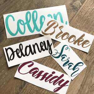 May include: Five custom name decals in various colors. Names include Colleen, Brooke, Delaney, Sarah, and Cassidy. The names are written in a cursive font with glitter accents. Each decal is on a white background.