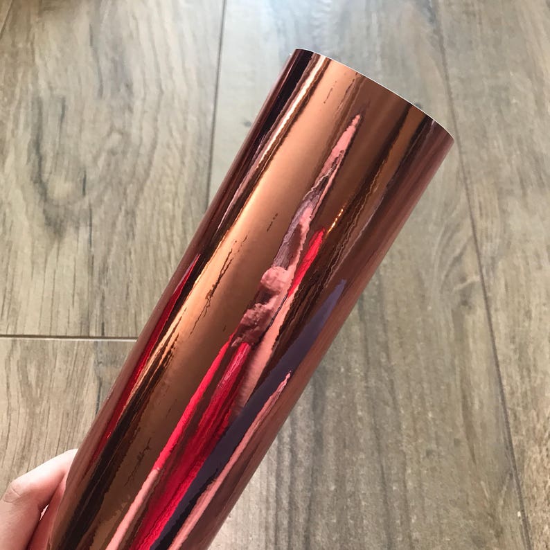 Rose gold adhesive chrome mirror vinyl sheet, held to display its reflective finish and color gradations from pale rose to deep burgundy
