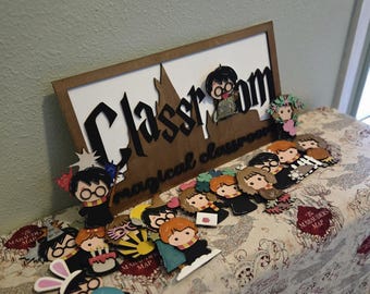 May include: A wooden sign with the words "Classroom" and "magical classroom" in black lettering. The sign is decorated with small, colorful paper cutouts of characters from the Harry Potter series, including Harry Potter, Ron Weasley, Hermione Granger, and others. The sign is sitting on a table with a brown and white patterned tablecloth.