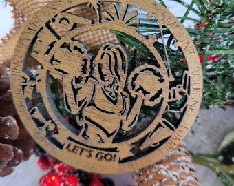 May include: A wooden Christmas ornament with a circular design. The ornament features a cutout image of a person and the text "LET'S GO!". The ornament is surrounded by pine needles, berries, and a pine cone.