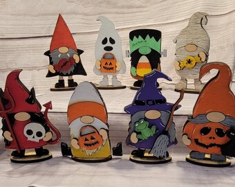 May include: Set of ten Halloween gnomes, each with a different costume and accessory. The gnomes are painted in various colors, including red, green, orange, purple, and white. They are all wearing hats and have white beards. The gnomes are holding various Halloween-themed items, such as candy corn, a pumpkin, a witch's broom, and a skull.