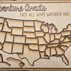 Puede incluir: Arte de pared de madera con un mapa detallado de los Estados Unidos, con cada estado cortado individualmente. Las palabras "Adventure Awaits" y "Not All Who Wander Are Lost" est&aacute;n cortadas con l&aacute;ser sobre el mapa. Hecho de madera marr&oacute;n claro.