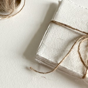 K&ouml;nnte beinhalten: Ein Stapel wei&szlig;er Papierbl&auml;tter, die mit Schnur zusammengebunden sind. Das Papier hat eine raue, strukturierte Oberfl&auml;che.