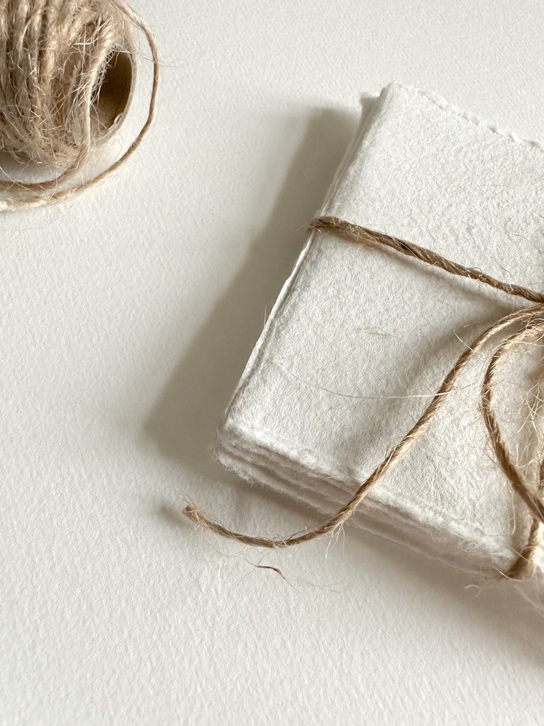 K&ouml;nnte beinhalten: Ein Stapel wei&szlig;er Papierbl&auml;tter, die mit Schnur zusammengebunden sind. Das Papier hat eine raue, strukturierte Oberfl&auml;che.